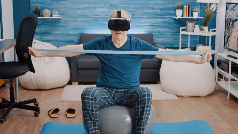 File:Aged-person-pulling-resistance-band-wearing-vr-glasses-while-sitting-toning-ball-home-retired-man-using-virtual-reality-headset-training-with-stretching-elastic-belt.jpg